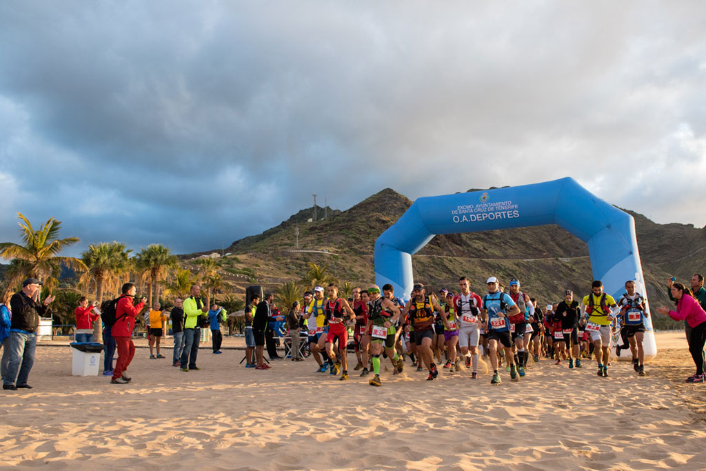 Runners starting a marathon on Las Teresitas beach, Tenerife, under a blue arch.