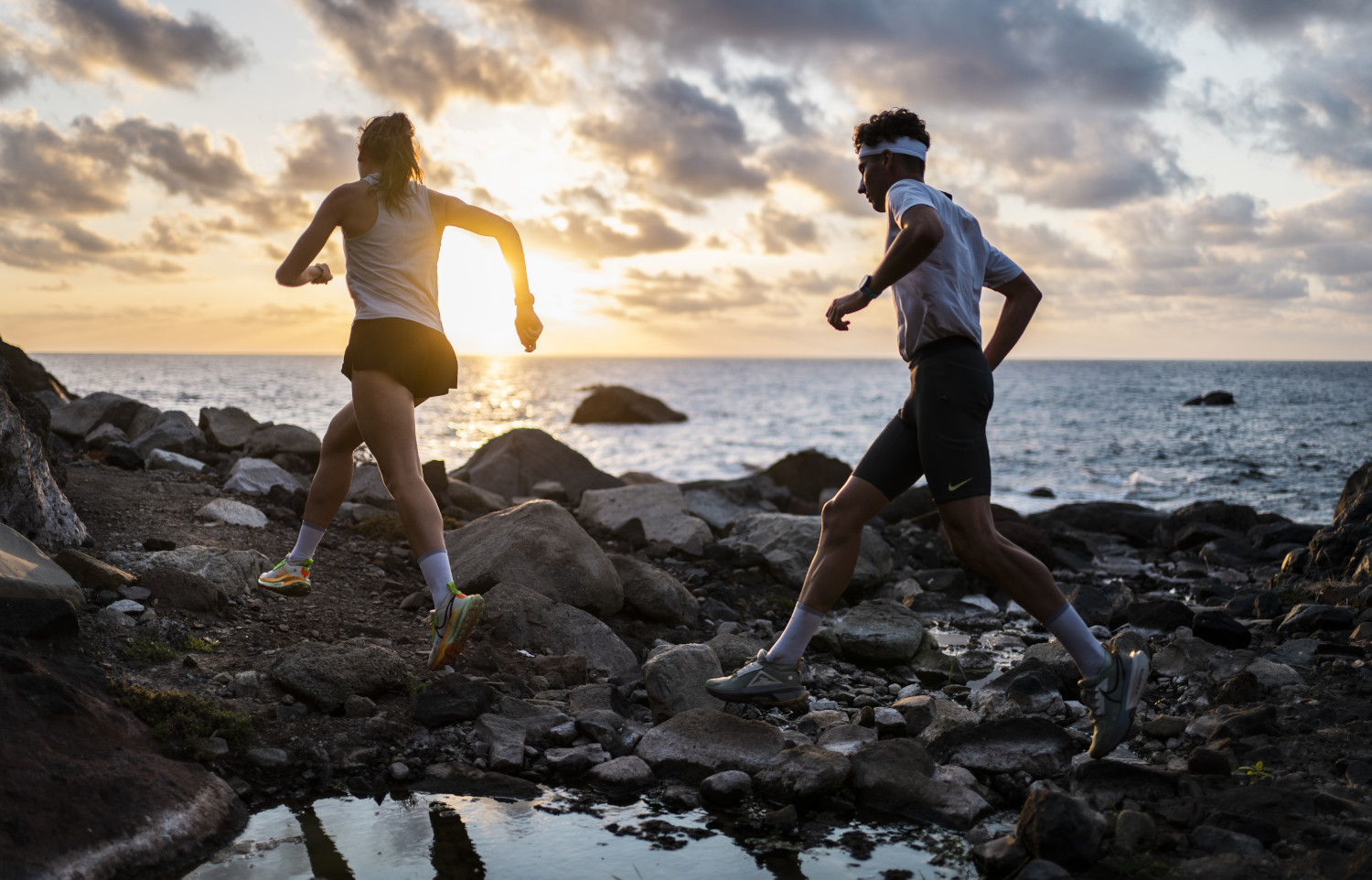 People running on the rocky coast of Tenerife at sunset.
