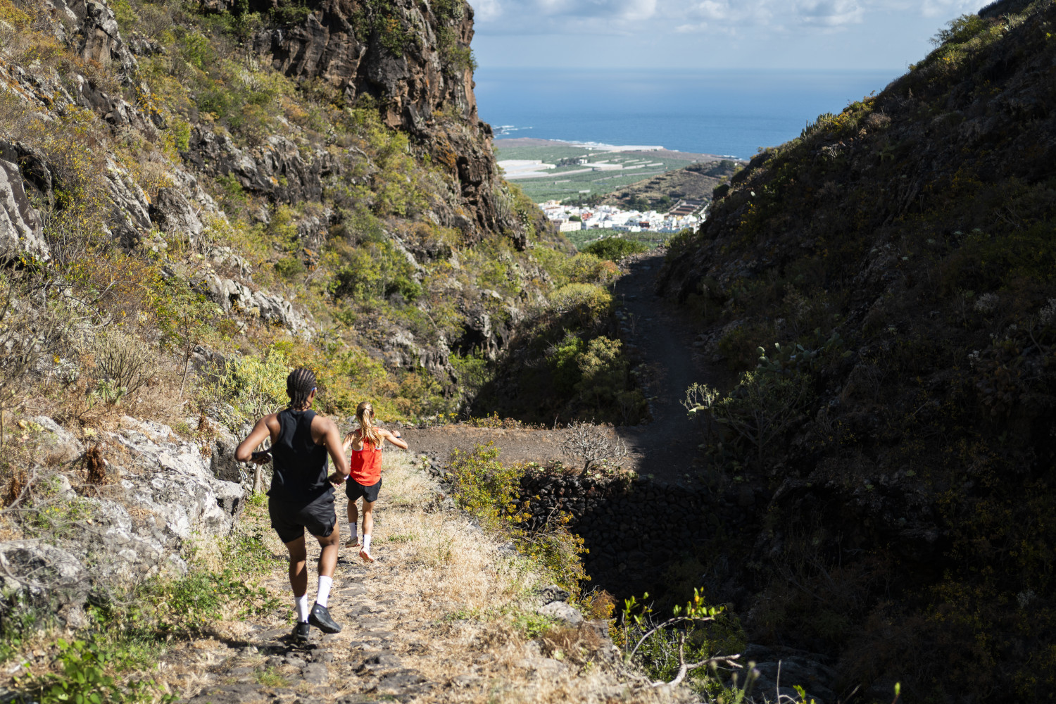 People running along a mountainous trail in Tenerife, overlooking the sea and the valley.