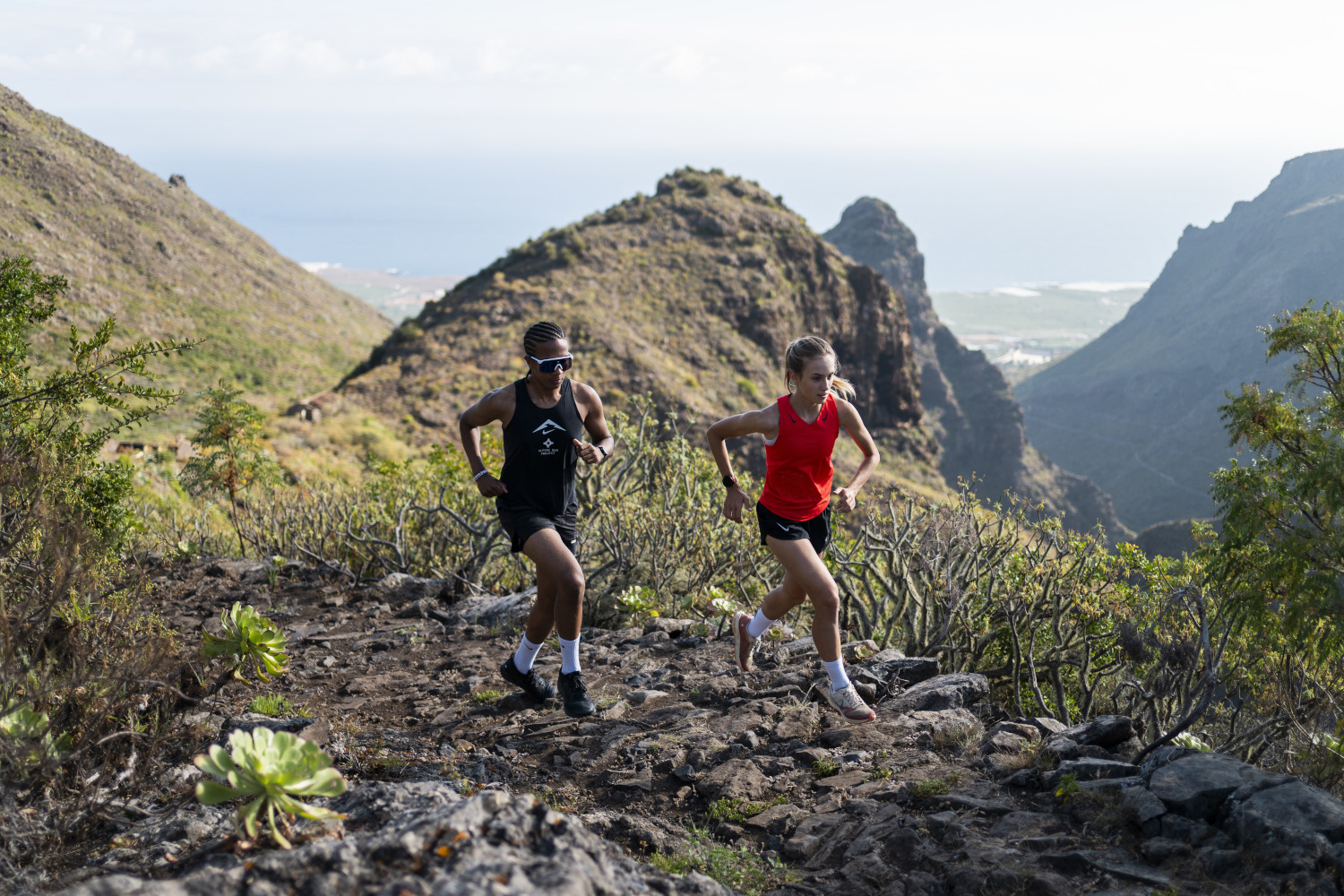 Two people running along a mountainous path in Tenerife with sea views.