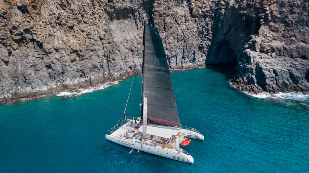 Catamaran sailing near rocky cliffs on the coast of Tenerife.