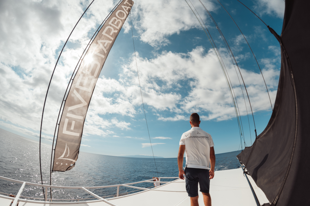 Person on the bow of a boat wearing a T-shirt that says FIVESTARBOAT, looking out to sea in Tenerife.