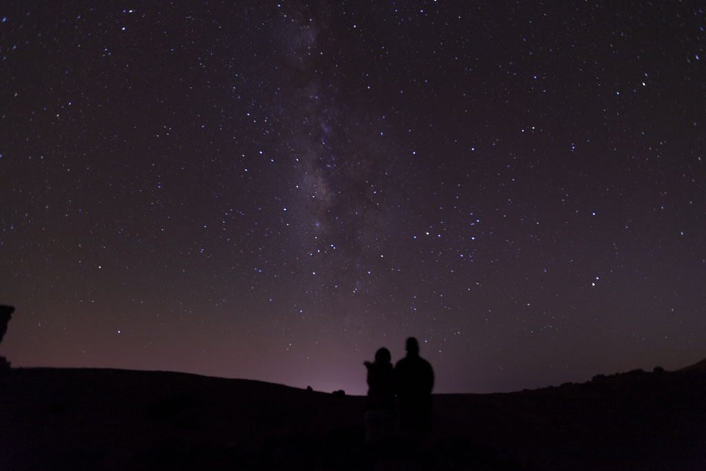 Starry sky over Mount Teide in Tenerife with two silhouettes watching.