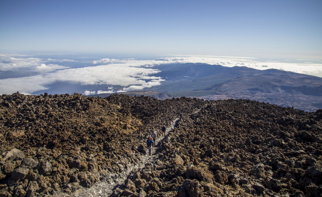 Hikers on the Teide trail, Tenerife, with clouds and mountains in the background.