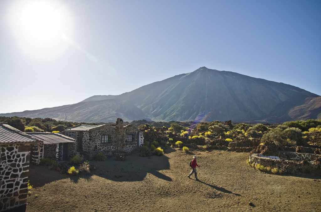 Person walking near stone houses with Mount Teide in the background in Tenerife.
