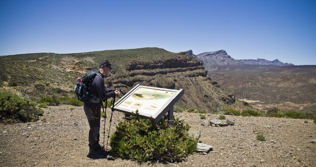 Person reading informative poster in Tenerife national park with mountainous landscape.