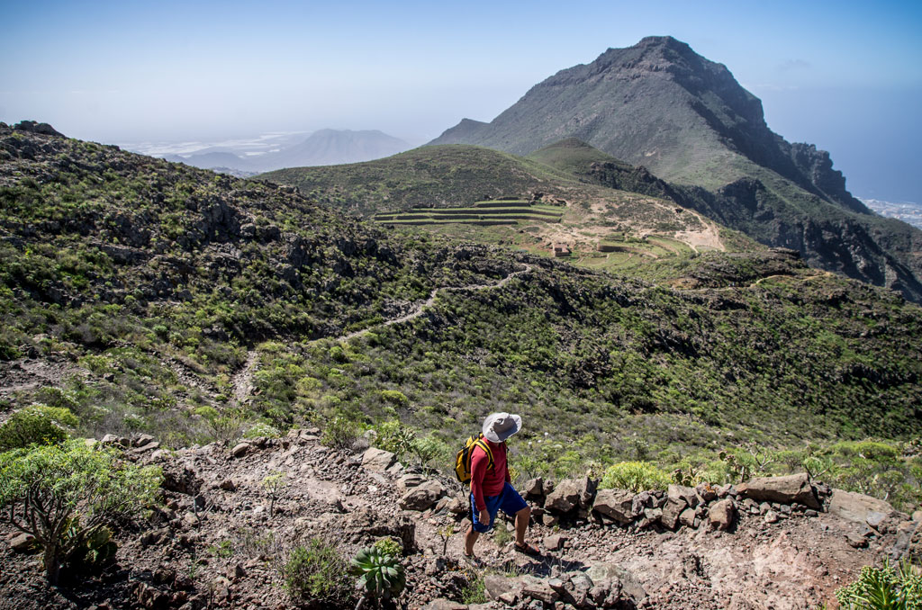 Hiker in the Teno massif, Tenerife, with mountains and terraces in the background.