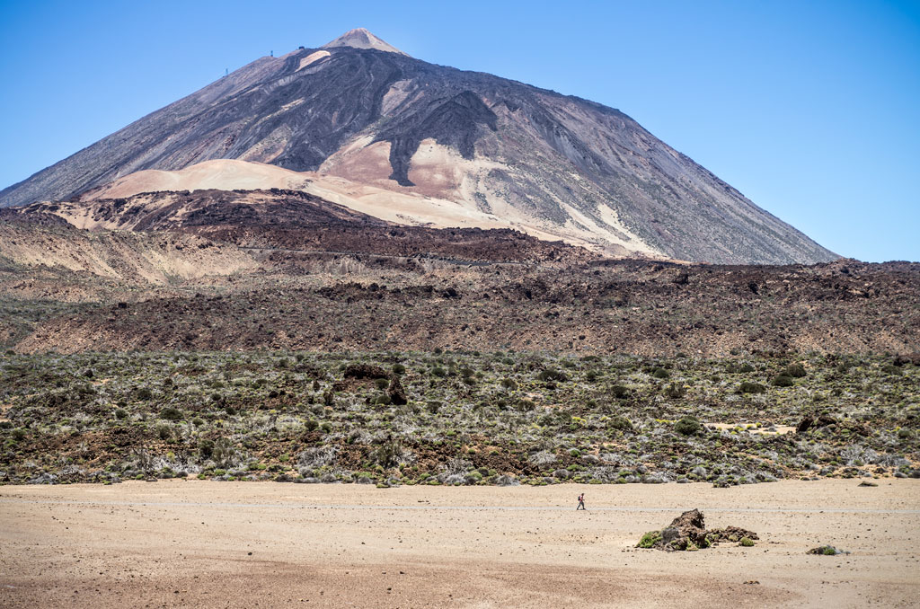 Mount Teide in Tenerife with volcanic landscape and a hiker in the background.