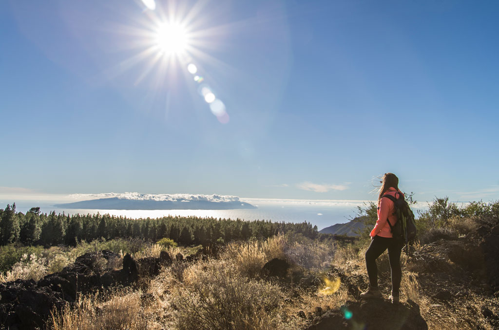 Person with backpack contemplating natural landscape in Tenerife under sunny sky.