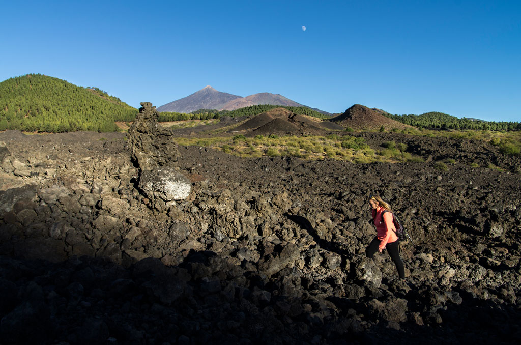 Person walking on volcanic terrain near Mount Teide, Tenerife, with clear skies.