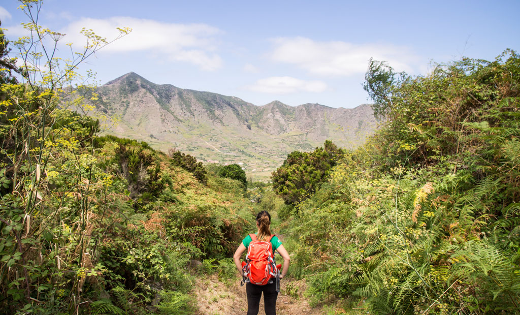 Person with red backpack walking on a trail in Anaga, Tenerife. Mountains in the background.
