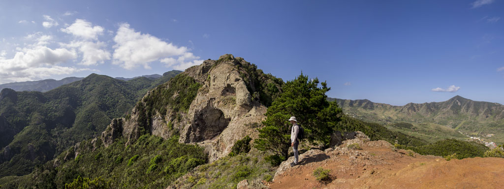 Person walking on a scenic trail in Anaga, Tenerife, surrounded by green mountains.