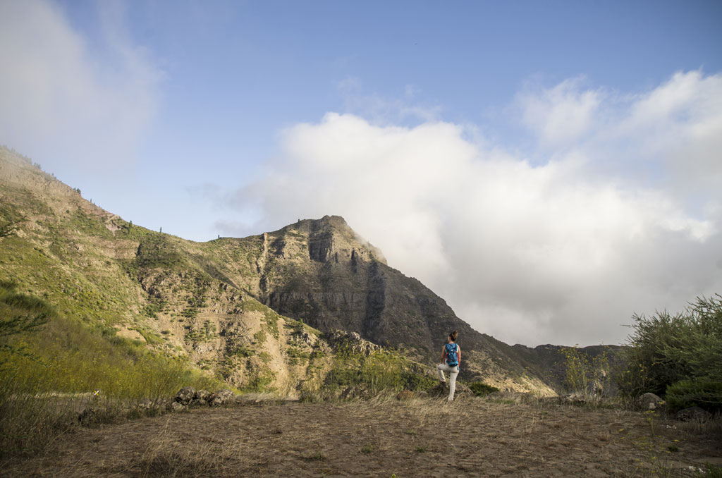 Person walking in front of mountains in Tenerife under partly cloudy skies.