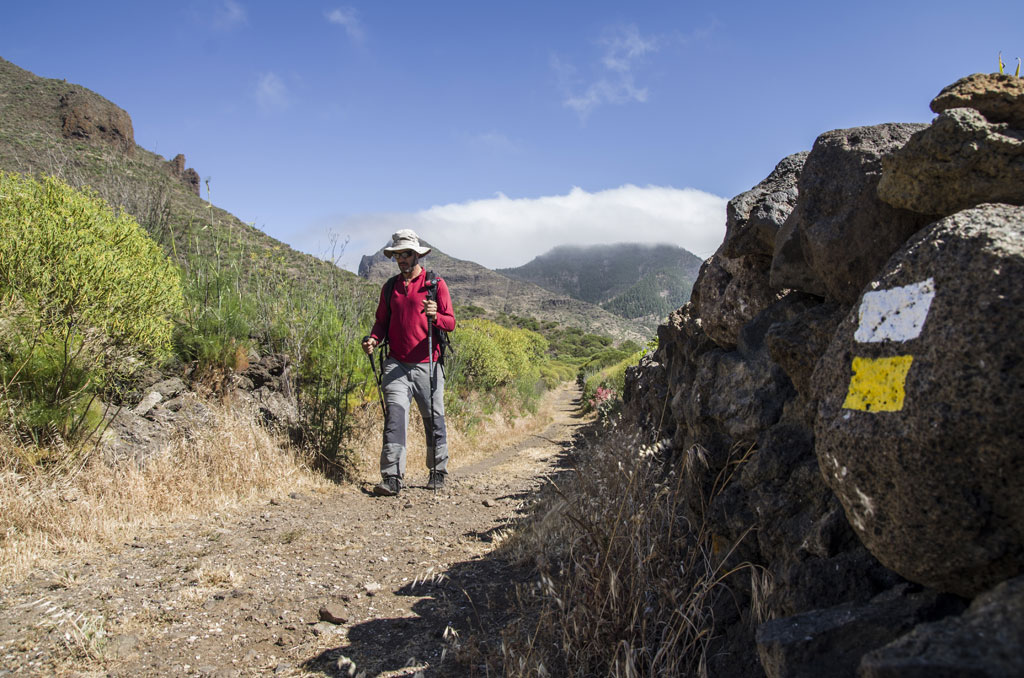 Person walking with a cane on a trail in Tenerife, mountains and rock signs.