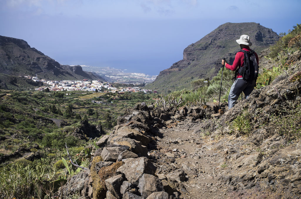Hiker with poles on a mountainous trail, view of Masca, Tenerife.