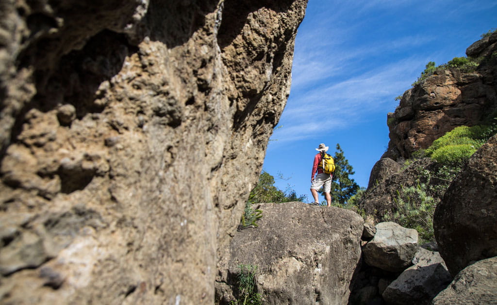 Person with yellow backpack on rocky trail in Tenerife under blue sky.