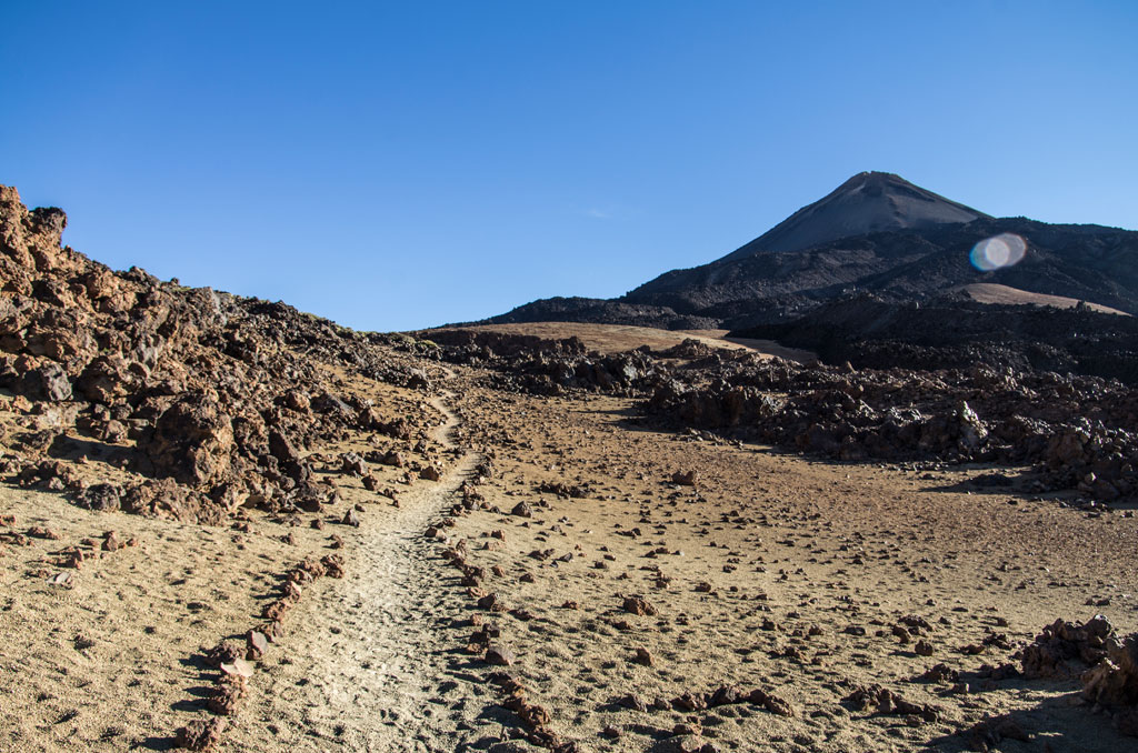 Rocky trail leads towards the Teide volcano under clear skies in Tenerife.
