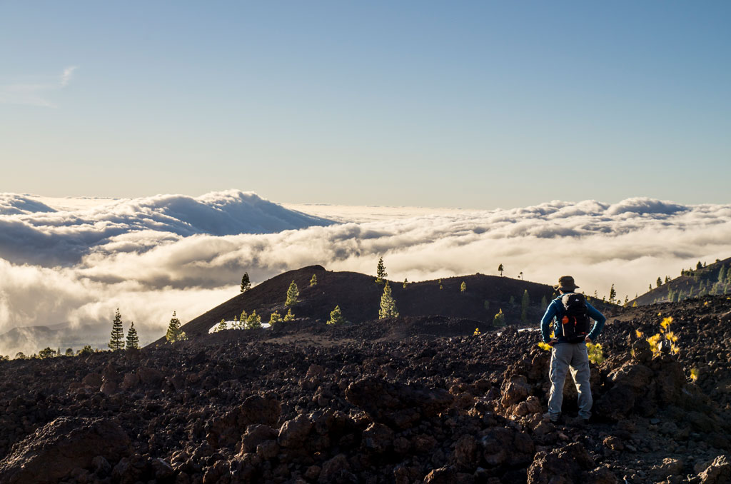 Trail in the volcanic landscape of Tenerife with walker and low clouds.