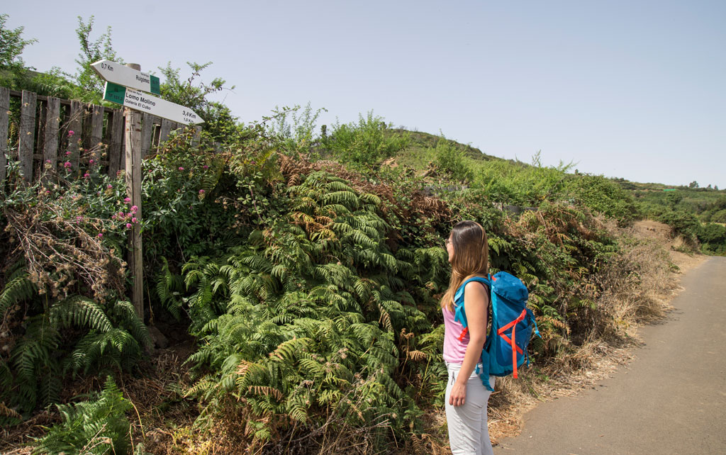 Hiker with backpack on trail to Lomo Molinos, sign 3.4 km in Tenerife.