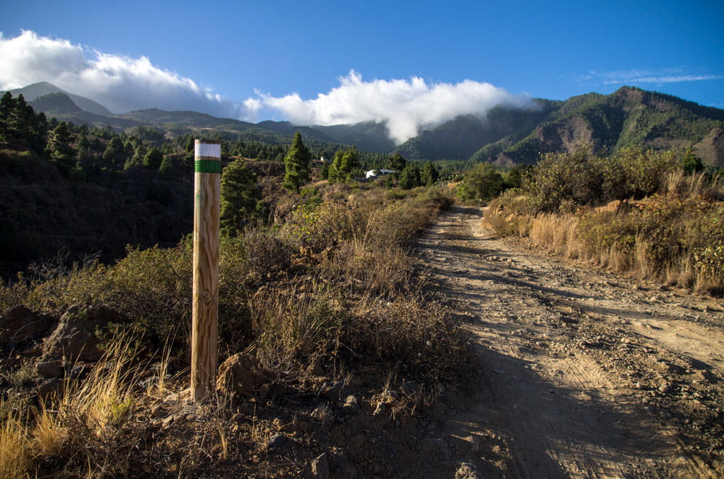 Dirt path with mountainous landscape in Tenerife, signpost on the left.