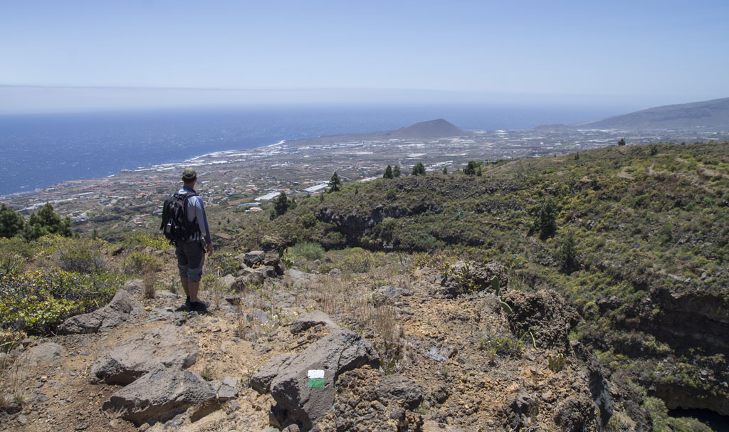 Person walking on a rocky path with a view of the sea and landscape of Tenerife.