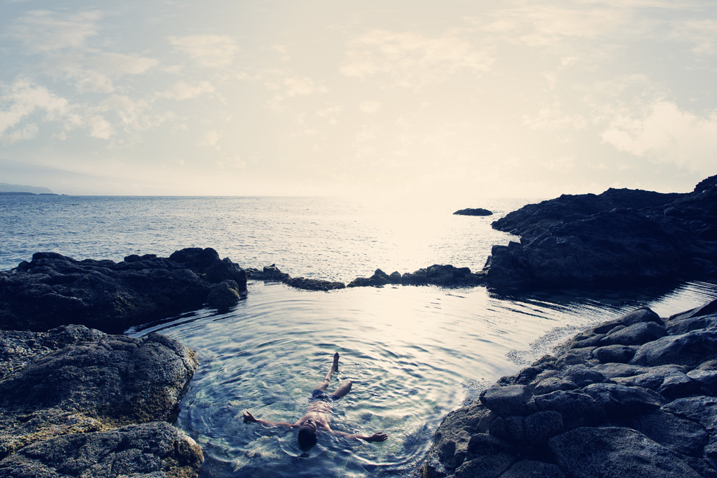 Person floating in a natural pool surrounded by rocks by the ocean in Tenerife.
