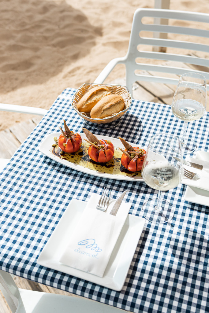Table with stuffed tomatoes, bread and glass of wine in front of El Ancla beach in Tenerife.
