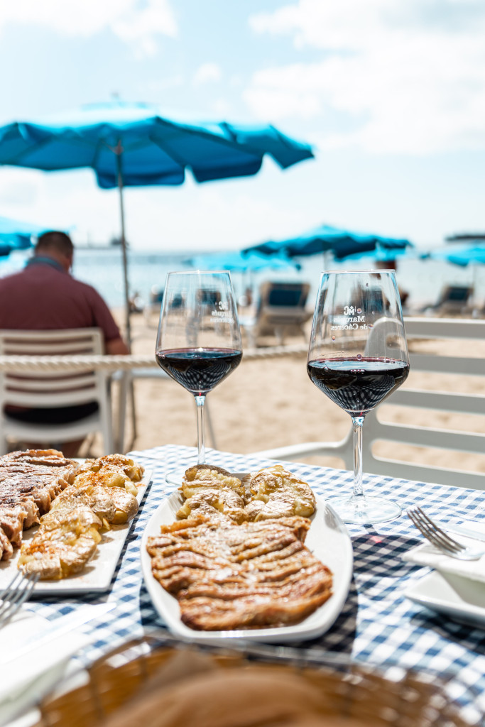 Glasses of wine and food on the beach with blue umbrellas in Tenerife.