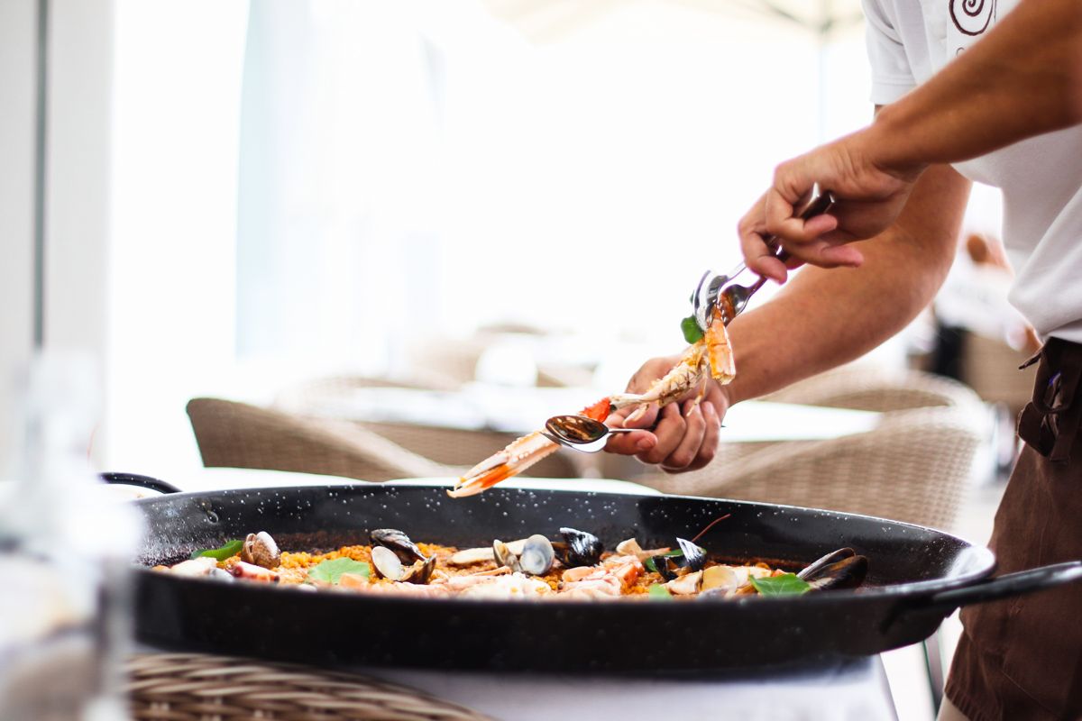 Person serving seafood in a paella on a restaurant terrace in Tenerife.
