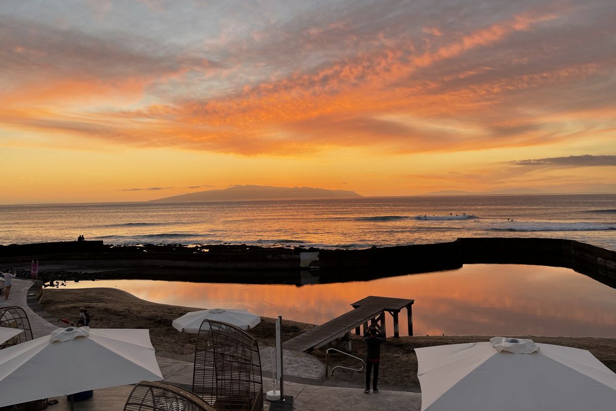 Sunset over the ocean in Tenerife with orange skies and umbrellas in the foreground.