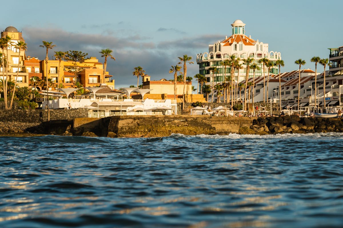 View of the coast of Tenerife at sunset with buildings and palm trees.