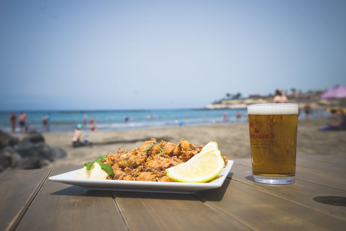 Plate of food and glass of drink on a table on a beach in Tenerife.