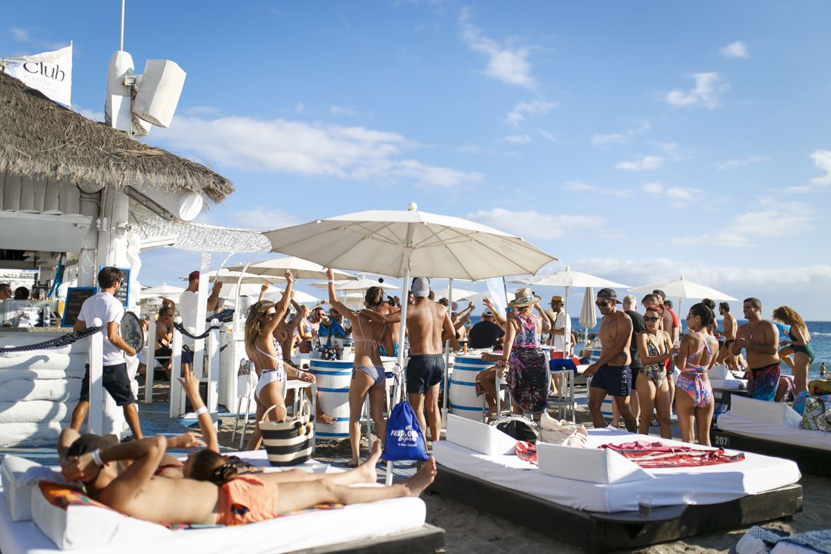 People enjoying a beach club in Tenerife under umbrellas.