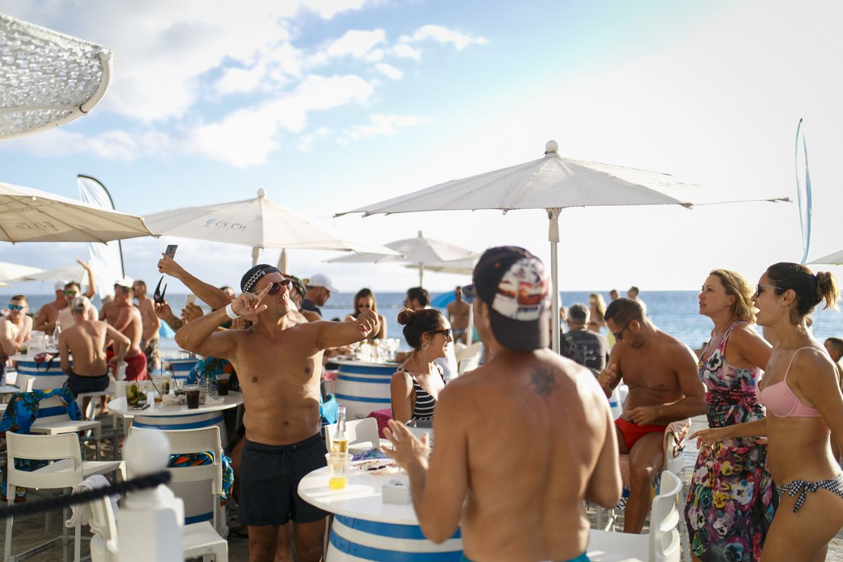 People enjoying a beach party in Tenerife, with umbrellas and tables.