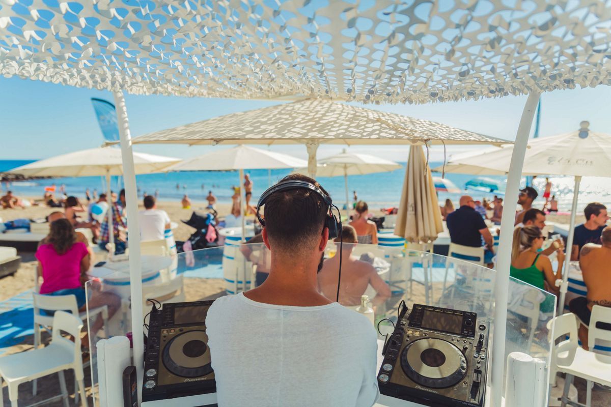 DJ playing music on a beach in Tenerife with people enjoying the sea.