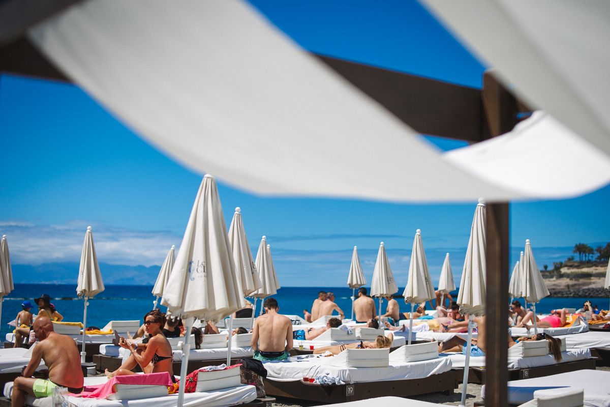 People sunbathing in hammocks under umbrellas on Tenerife beach.