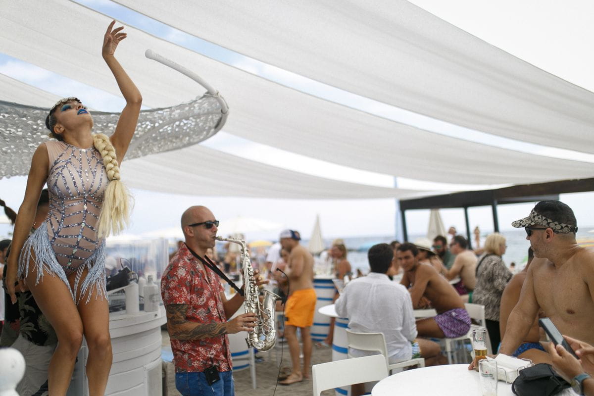 Dancer and musician playing saxophone at outdoor event on Tenerife beach.