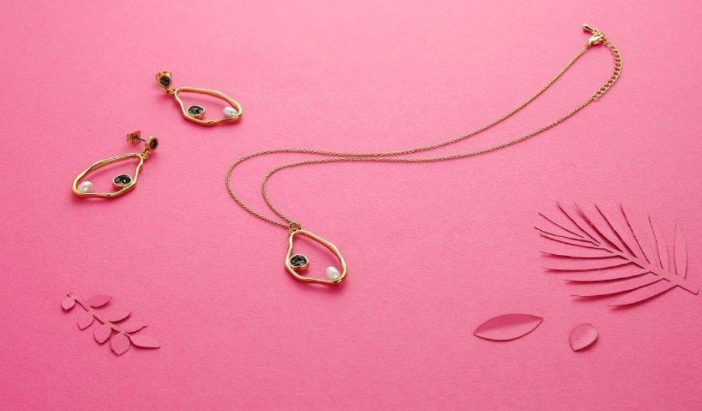 Gold necklace and earrings with pearls on a pink background and leaf decorations.