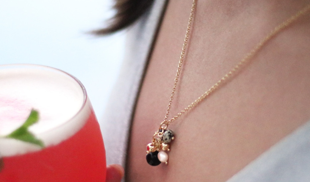 Necklace with pendants and pink drink in a glass with a person.