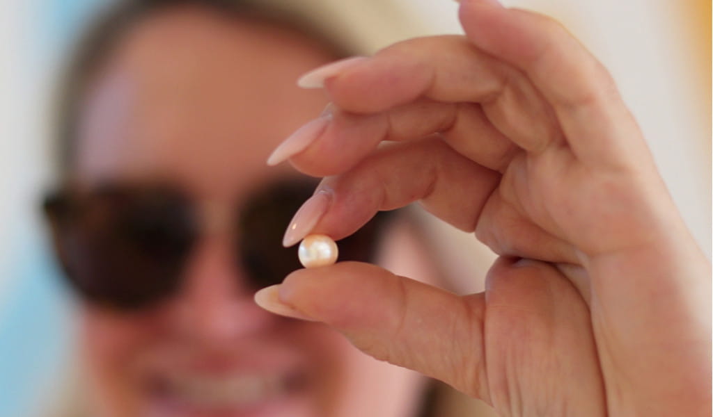 Hand holding a pearl with person out of focus in the background.