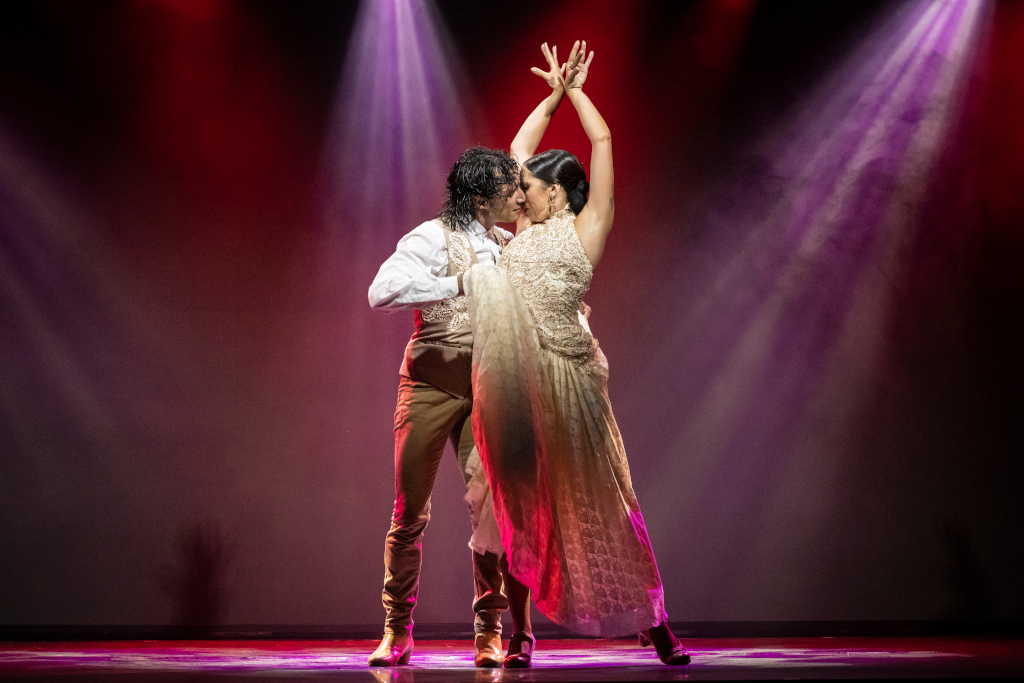Couple dancing flamenco under bright lights on a stage.