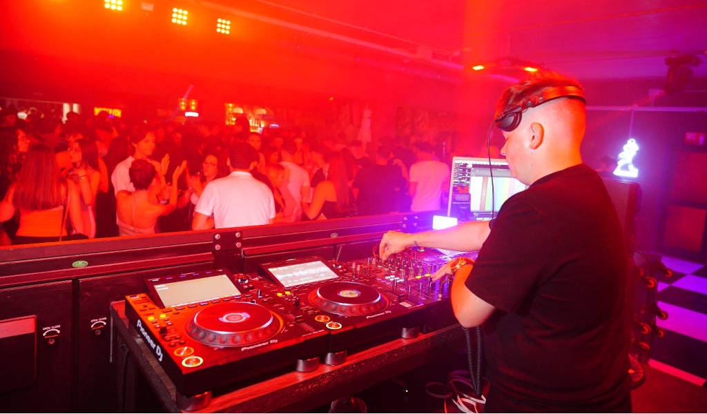 DJ animating party in nightclub in Tenerife with red lights and dancing audience.