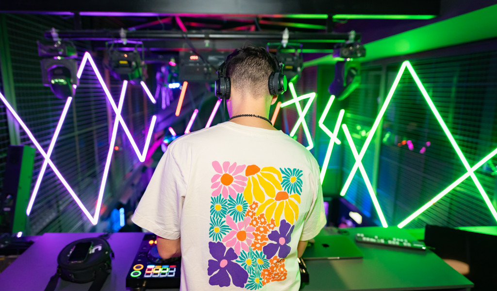 DJ in a floral t-shirt mixes music in Tenerife's club with neon lights.