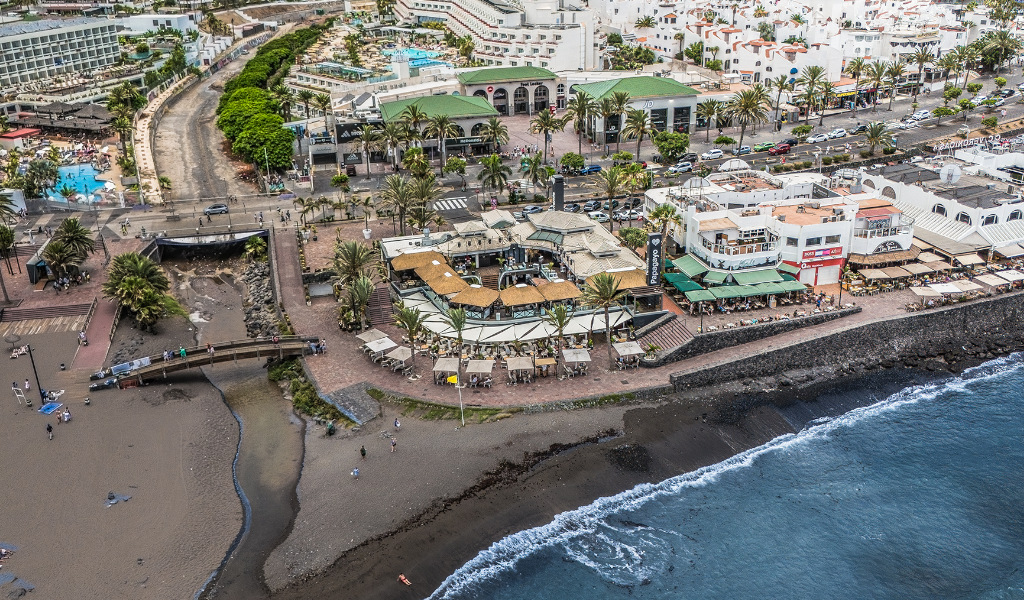 Aerial view of beach and urban area in Tenerife with buildings and restaurants nearby.