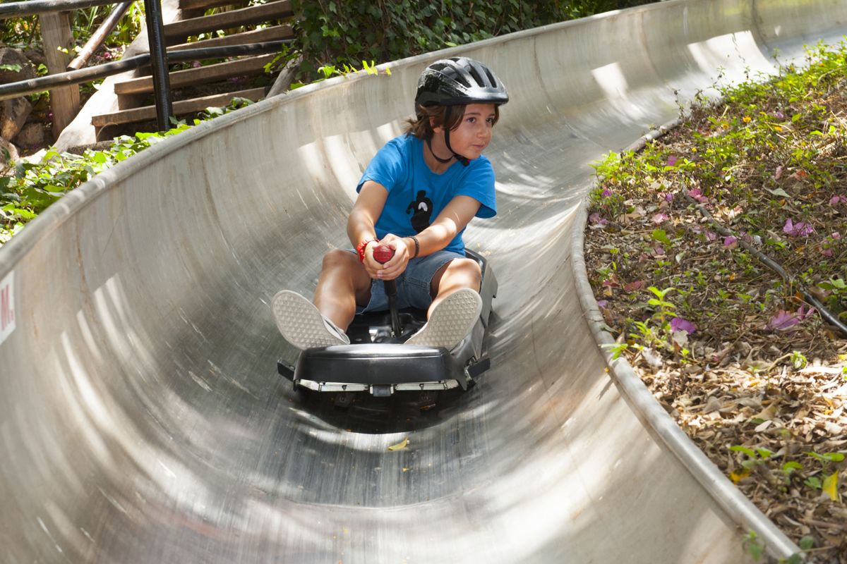 Boy with black helmet sliding on curved metal slide in Tenerife.
