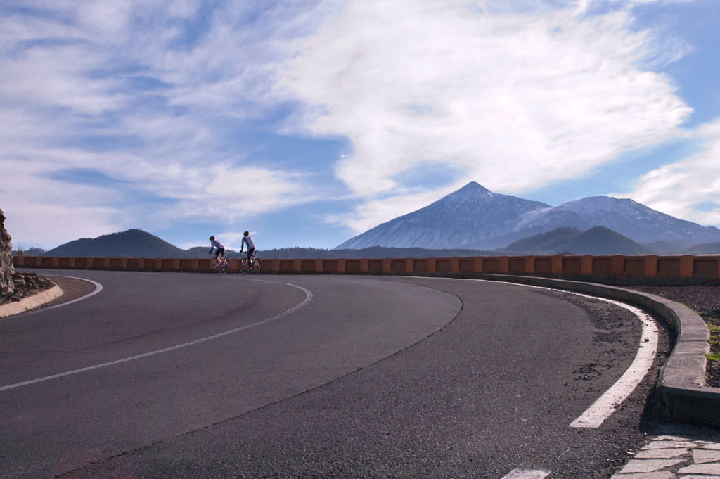 Cyclists ride along the road with views of Mount Teide in Tenerife.