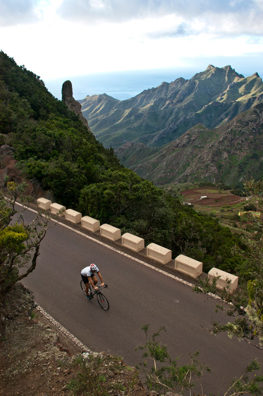 Cyclist on mountain road in Anaga, Tenerife, with sea and mountain views.