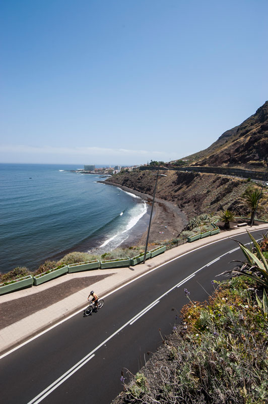 Cyclist on Tenerife coastal road with sea view and cliffs.