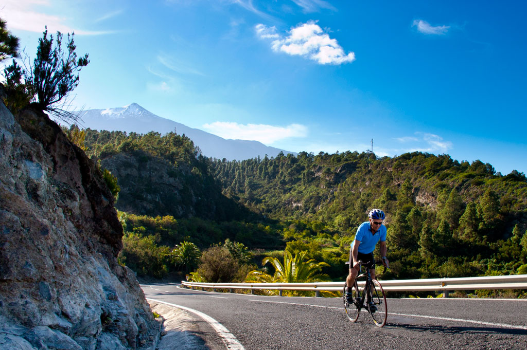 Cyclist on the road surrounded by mountains and vegetation, with a view of Mount Teide in Tenerife.
