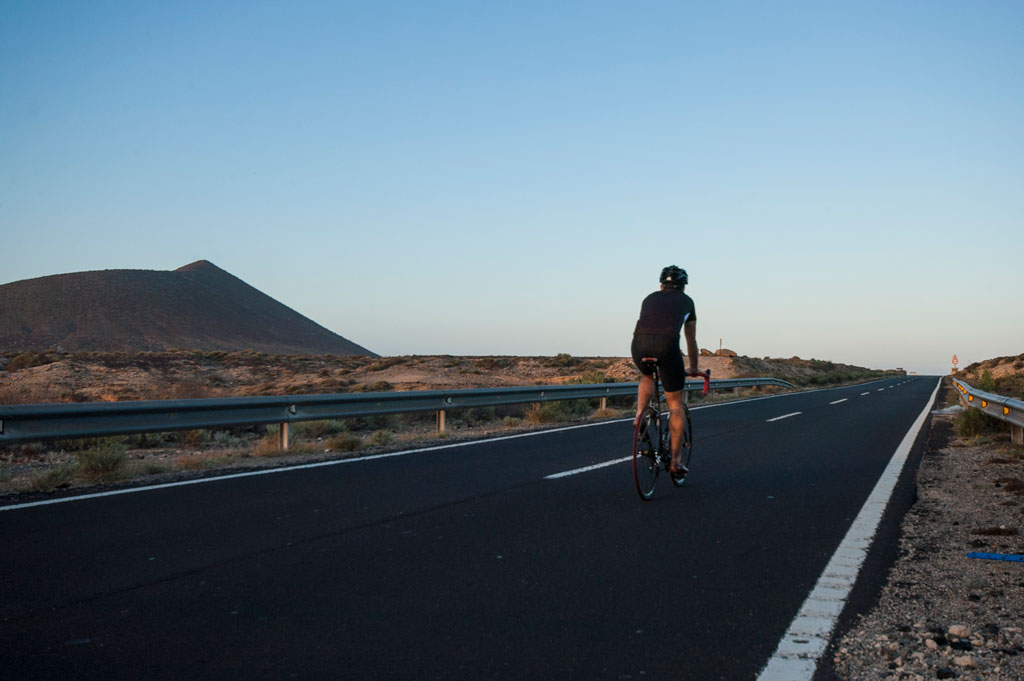 Cyclist on the road near a volcano in Tenerife at sunset.